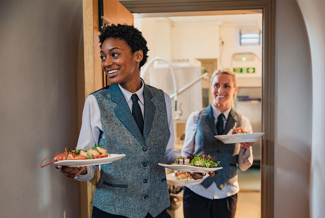 Two hospitality apprentices serving food